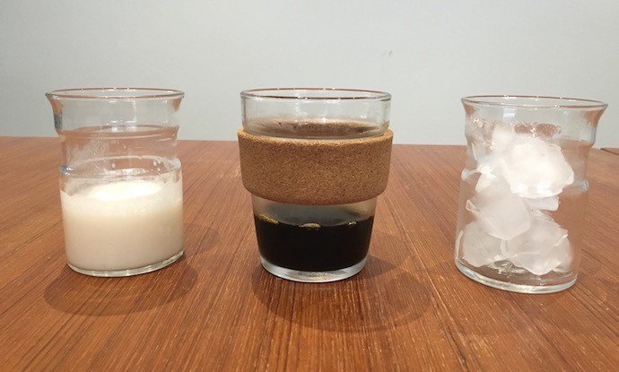three glasses with milk, cold brew and ice lined up on a table