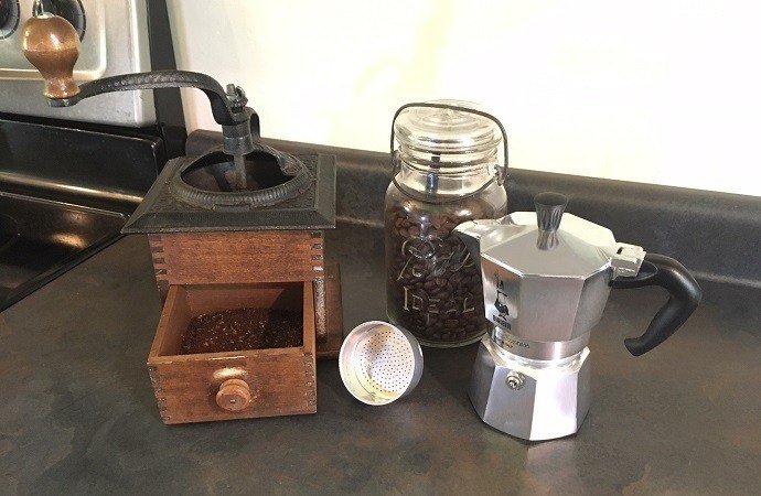 a hand grinder, a coffee bean container, and a stovetop coffee maker