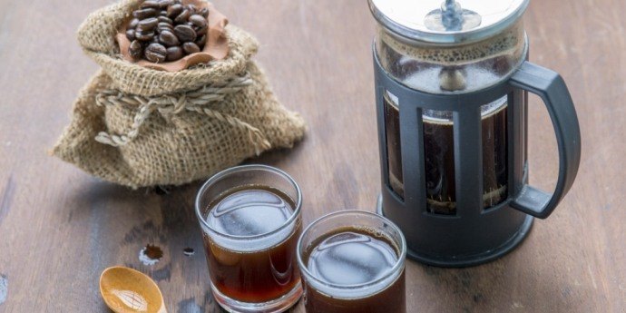 French press filled with coffee and two glasses on a wooden counter