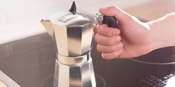 hand holding Moka pot on an electric stove