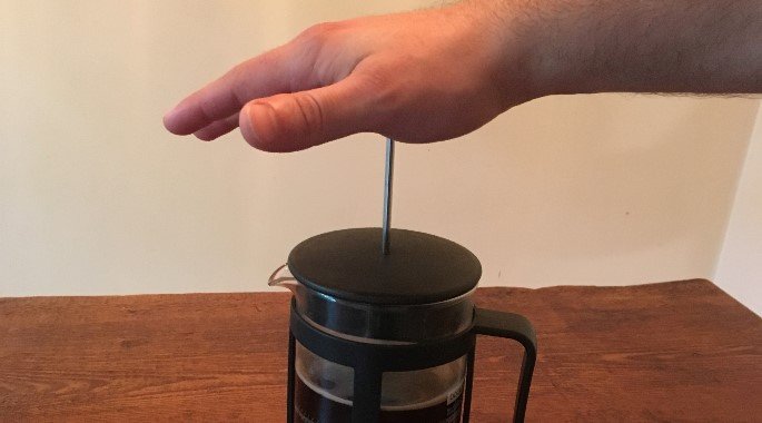 pushing the metal stick into the pot to make French Press coffee
