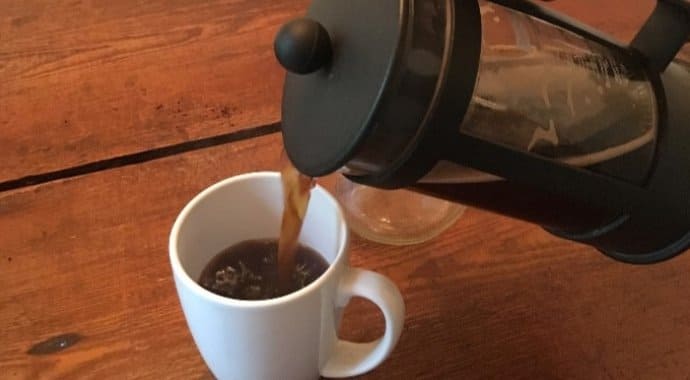 pouring hot French press coffee from a pot to a cup
