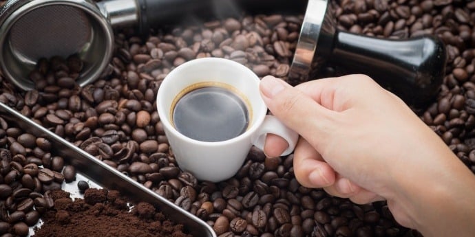 hand holding cup of brewed black coffee surrounded by coffee beans