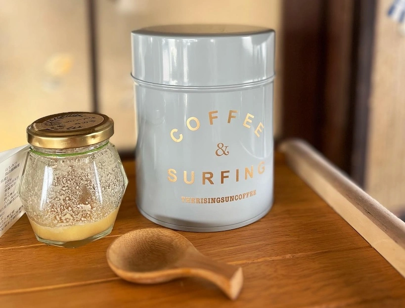 Blue coffee storage container next to a honey jar and a wooden spoon.