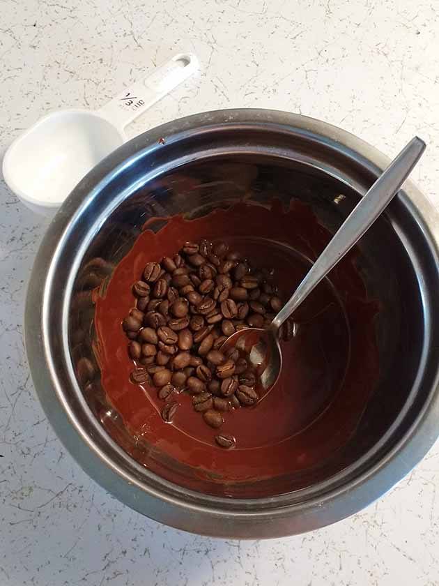 a spoon, melted chocolate, and asome coffee beans in a bowl