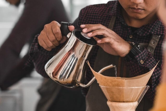 a man pouring water from a gooseneck kettle for making coffee