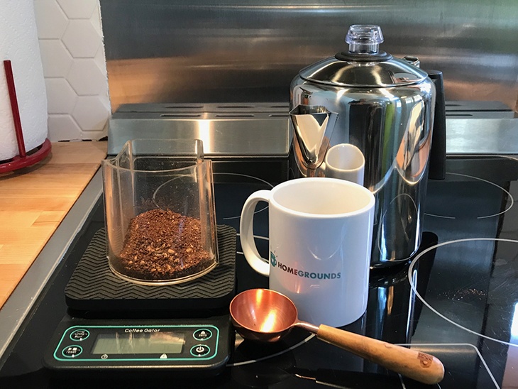 A stovetop percolator coffee grounds, a scale, a mug, and a measuring spoon