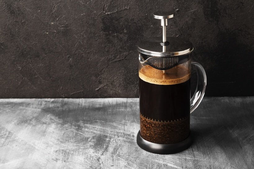 French press filled with coffee on a stone counter top