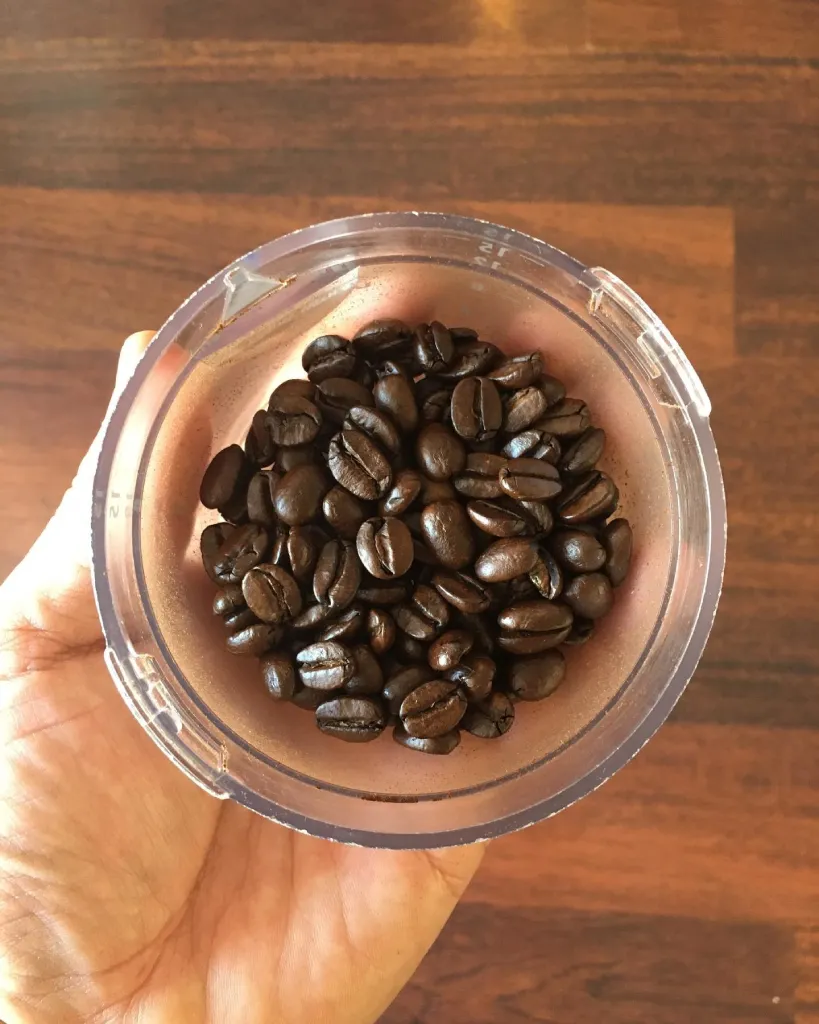 Person holding Kona coffee beans in a plastic cup