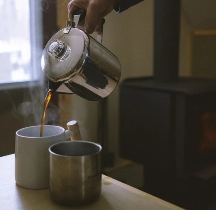 Hand pouring coffee from percolator into mugs