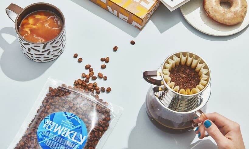 coffee beans spilled out the bag, cup of coffee with milk and a hand holding dripper